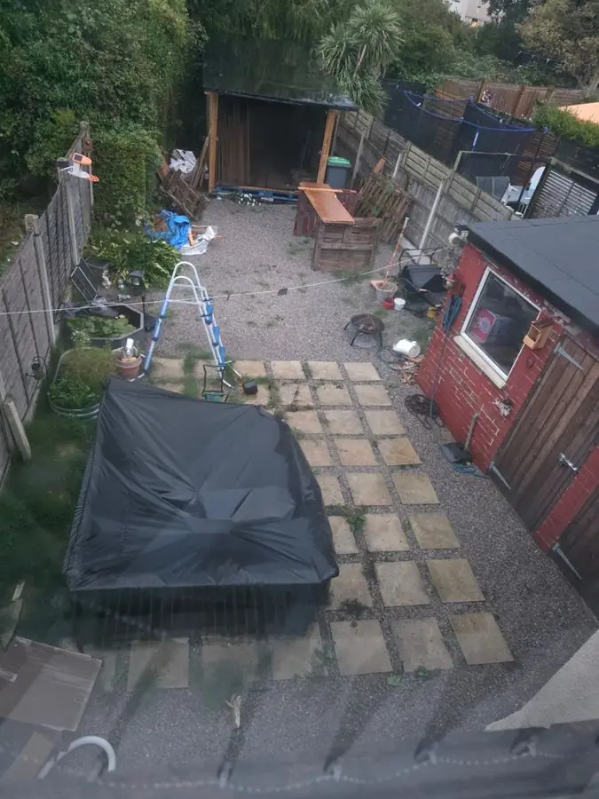 A cluttered yard with loose slabs, a tarpaulin and a shed, before the redesign