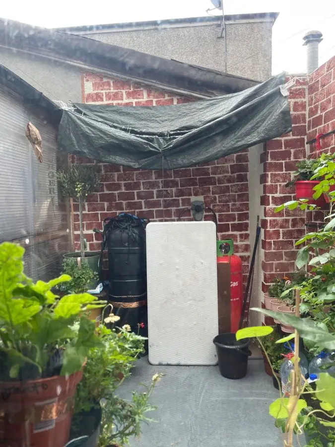 A small paved yard cluttered with a tarp, pots and boards, before the redesign
