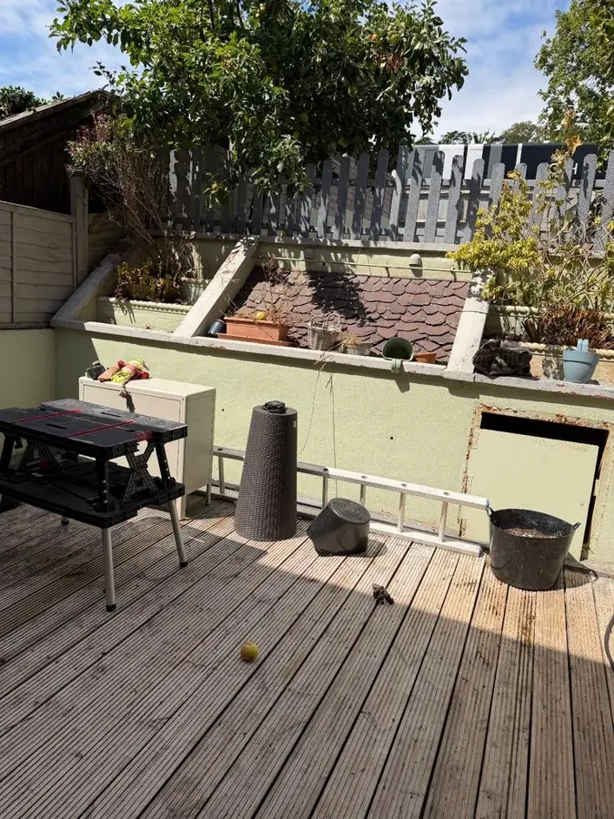 Raised decking with a picnic table, rendered raised beds and clutter behind, before the redesign