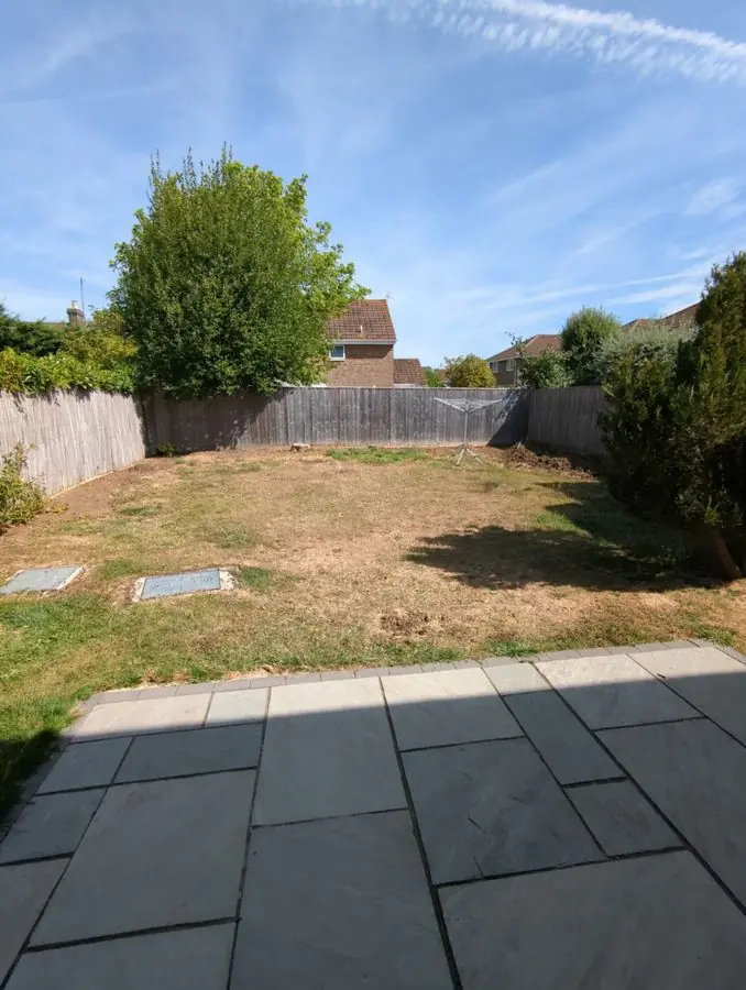 A patchy dry lawn behind a grey slab patio, before the redesign