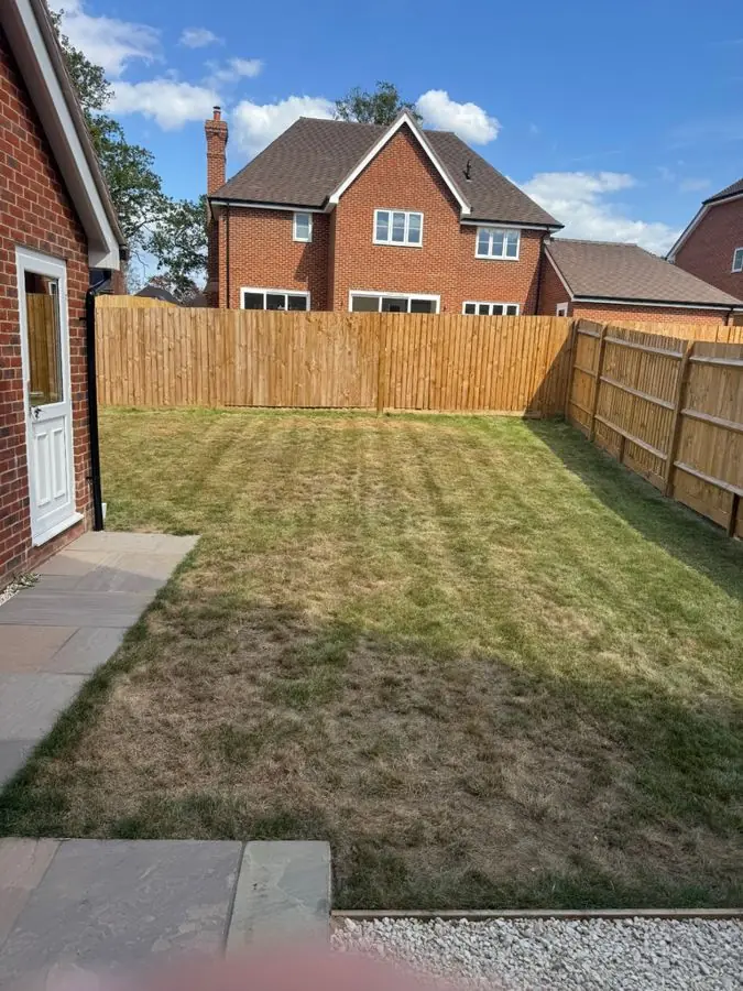 A plain striped lawn with a new wooden fence and side path, before the redesign