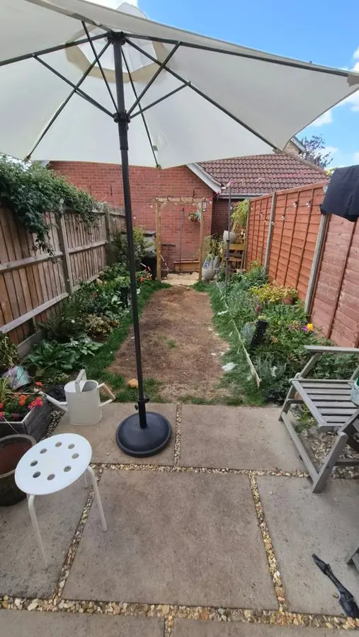 A slab patio with a parasol and a bare strip between fences, before the redesign