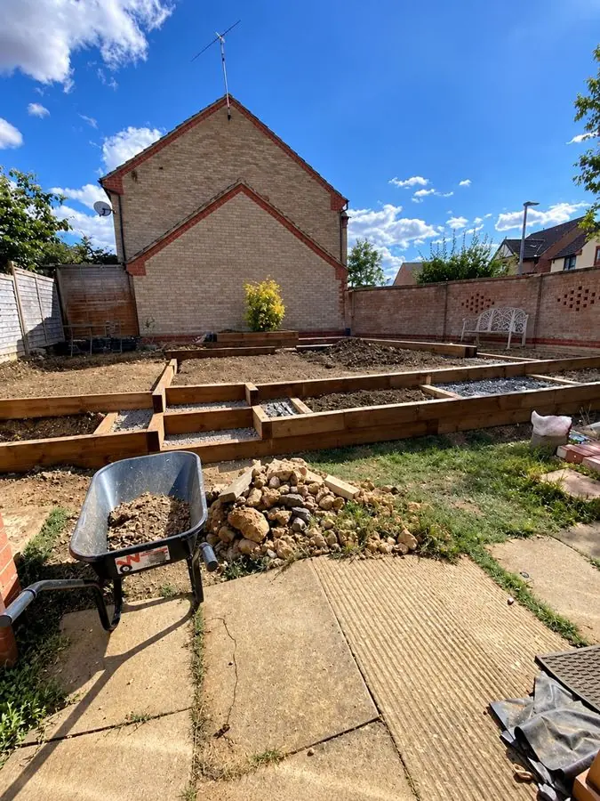 Empty raised beds, a wheelbarrow and rubble on cracked concrete, before the redesign