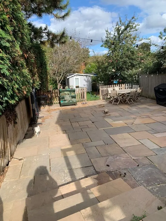 A large stone patio with a dining set at the far end, before the redesign
