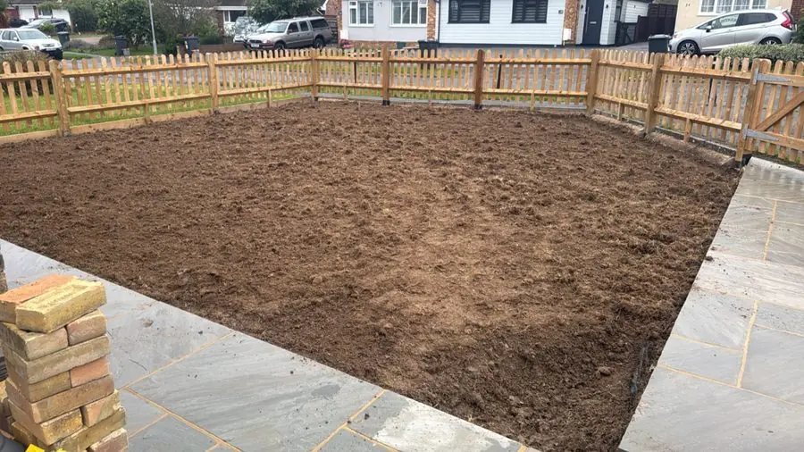 Bare soil inside a new picket fence with paving round it, before the redesign