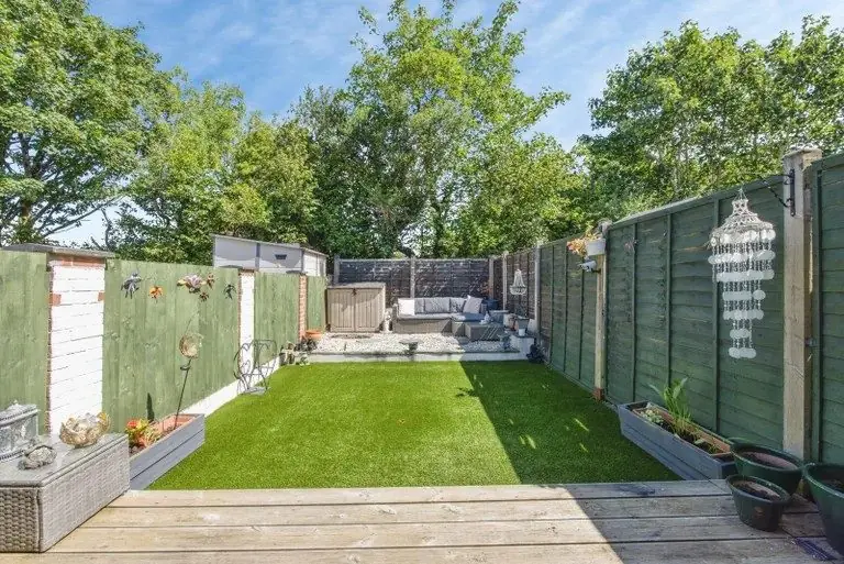 A narrow lawn between green fences with decking at the front, before the redesign