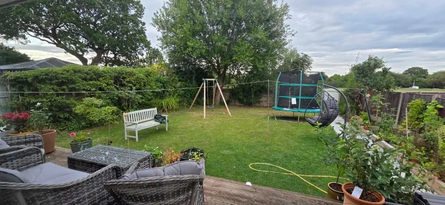 A family lawn with a swing, trampoline and garden sofas on a deck, before the redesign