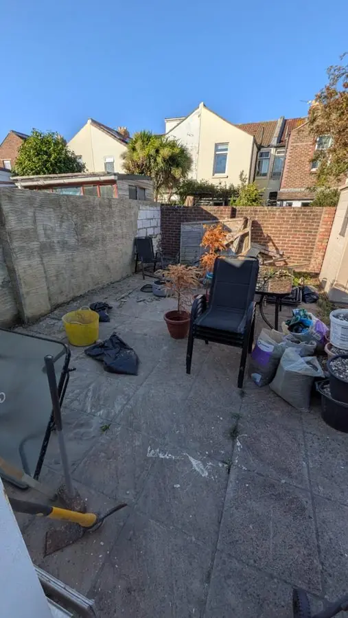 A cluttered paved yard with a chair and a block wall, before the redesign