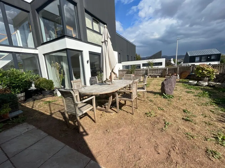 Bare earth with a dining table and parasol by a modern house, before the redesign