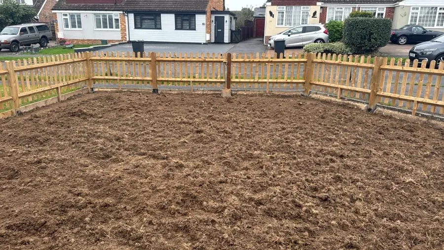 Bare raked soil inside a wooden picket fence facing the road, before the redesign