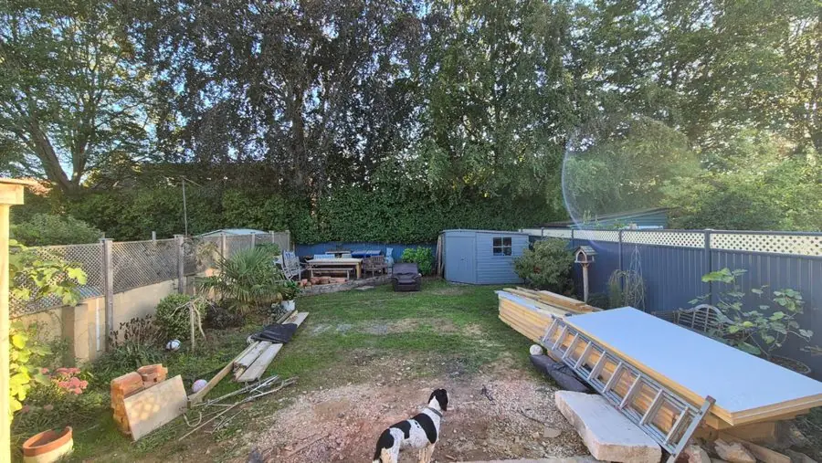A patchy lawn with building materials, a blue shed and fence, before the redesign