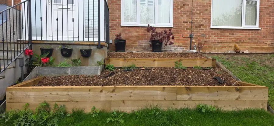 An empty wooden raised bed of soil under a window, before the redesign