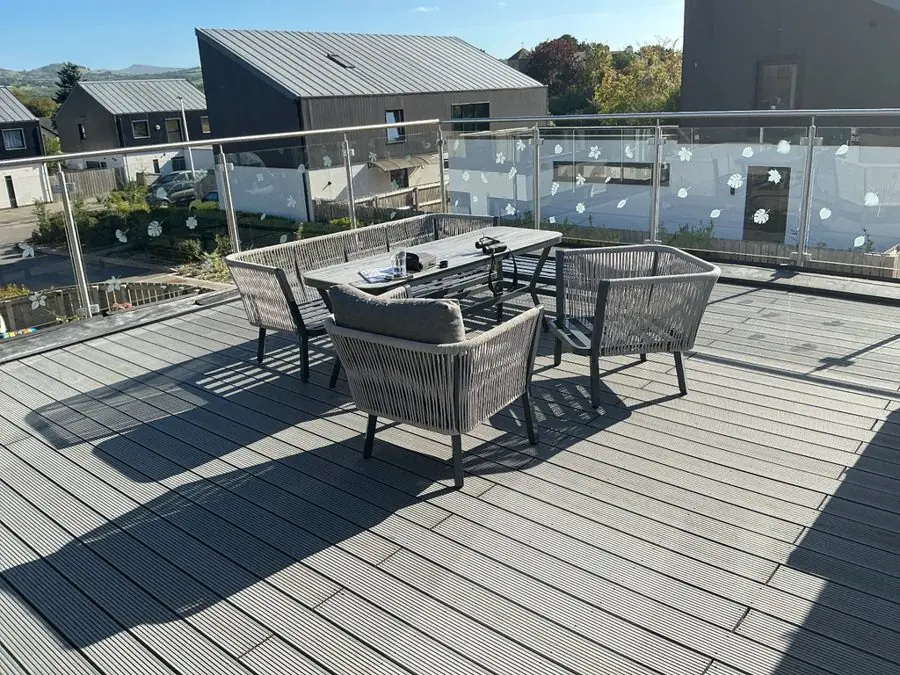 A decked roof terrace with grey outdoor furniture and glass railings, before the redesign