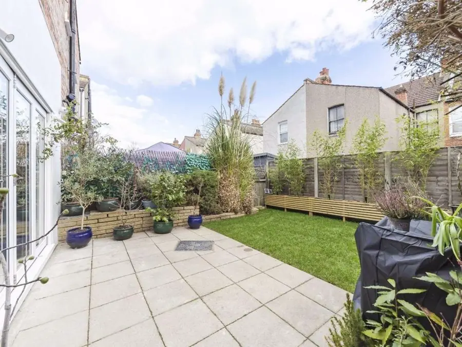A pale paved patio and small lawn beside raised timber beds, before the redesign