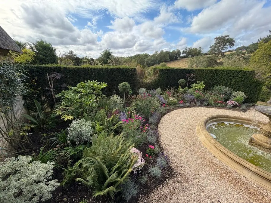A curved gravel path round a mixed border beside a stone fountain, before the redesign