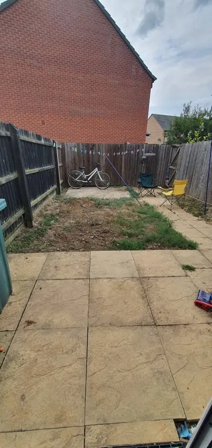 An old slab patio and scrappy lawn by a brick gable end, before the redesign
