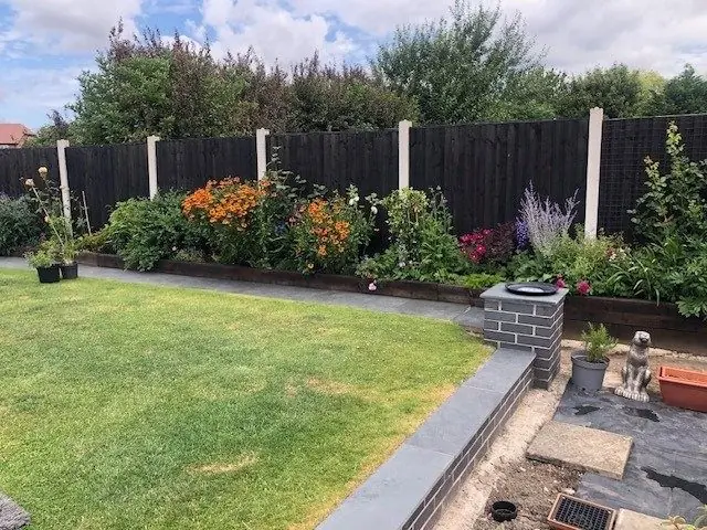 A lawn with a border of orange flowers along a dark fence, before the redesign