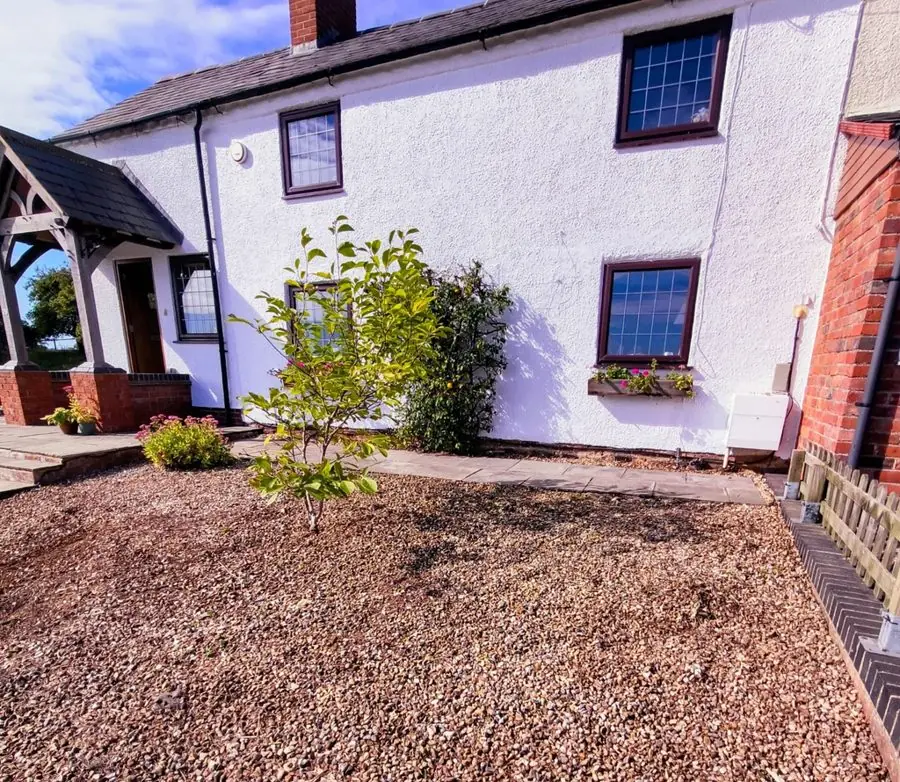 A bare gravel front garden in front of a white cottage, before the redesign
