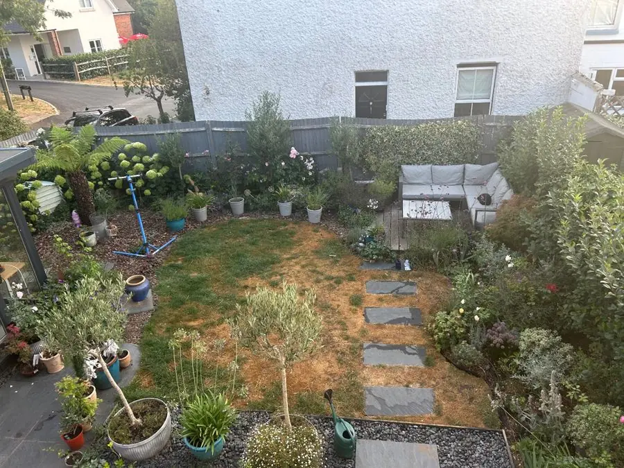 A patchy brown lawn with stepping stones, pots and a corner sofa, before the redesign