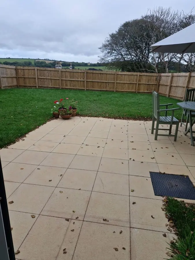 A plain stone patio and lawn with a wooden fence and table, before the redesign
