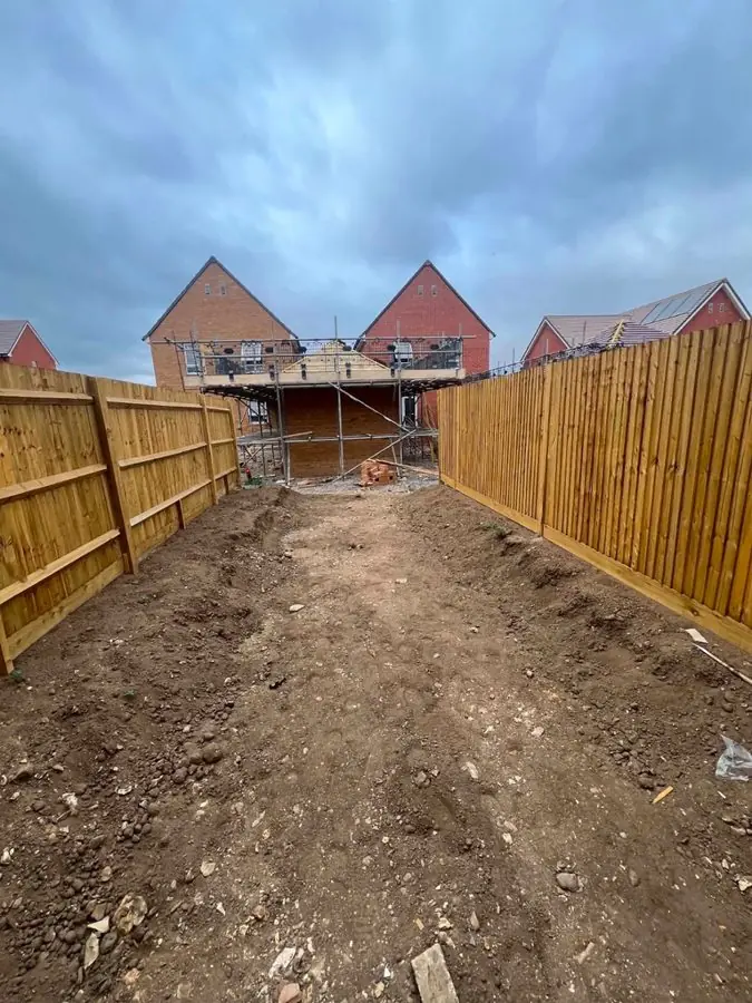 A bare earth plot between new wooden fences beside a building site, before the redesign