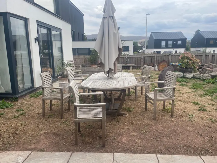 A wooden table and chairs on bare earth beside a modern house, before the redesign