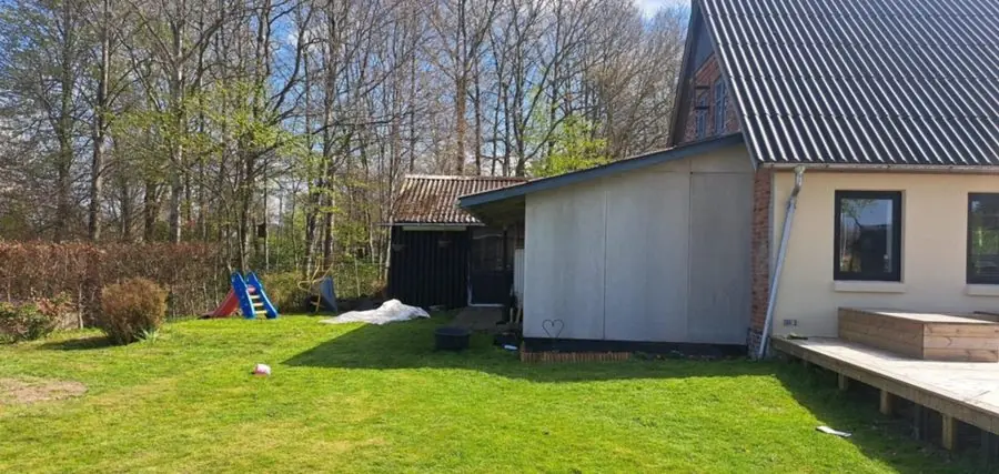 A plain lawn beside a house and shed with trees behind, before the redesign