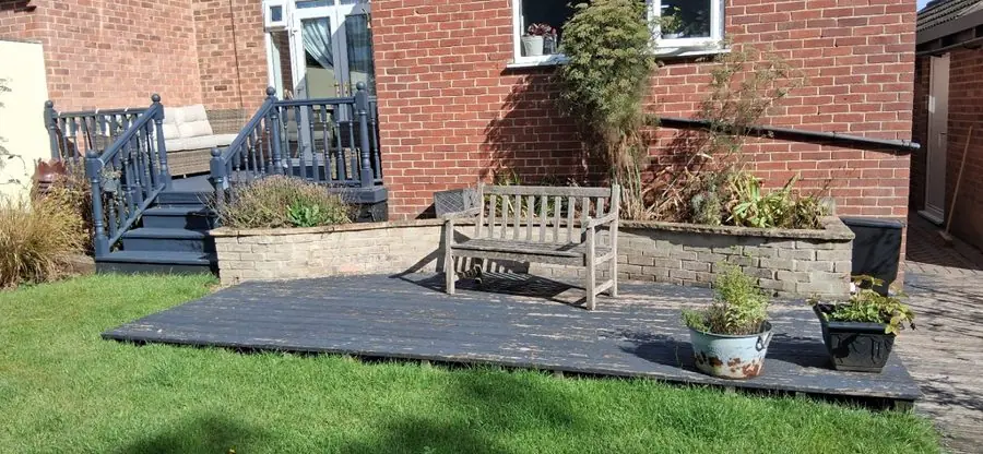 A dark timber deck on a lawn in front of a brick house, before the redesign