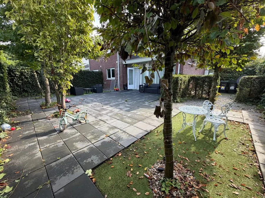 A paved patio and small lawn with a tree and white table, before the redesign