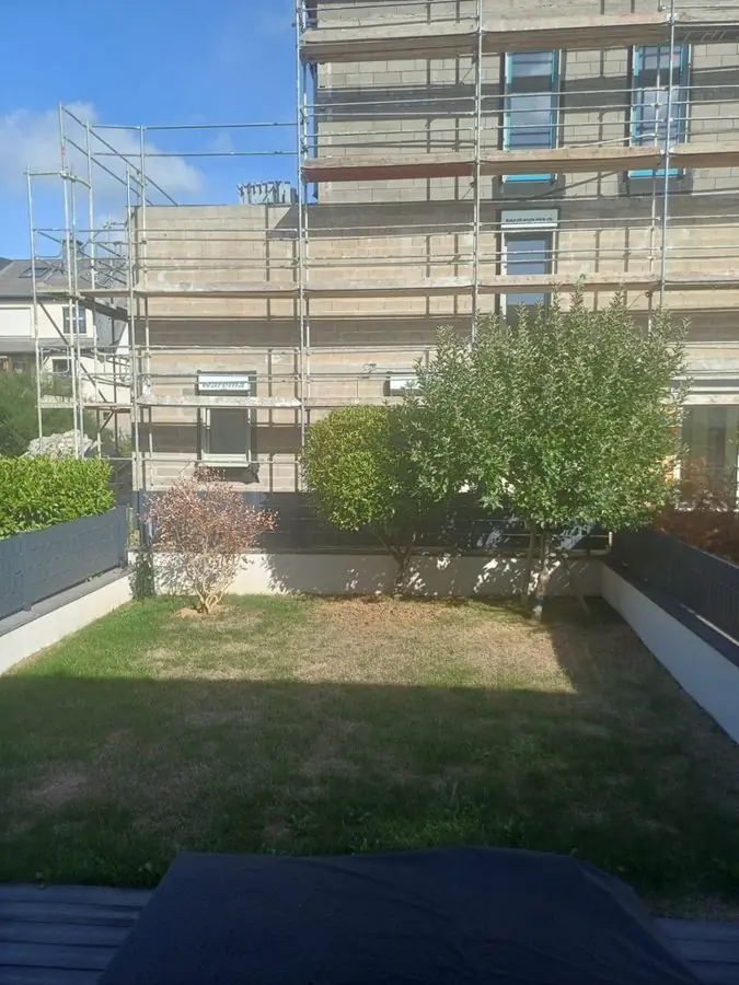 A plain lawn with low walls below a building under scaffolding, before the redesign