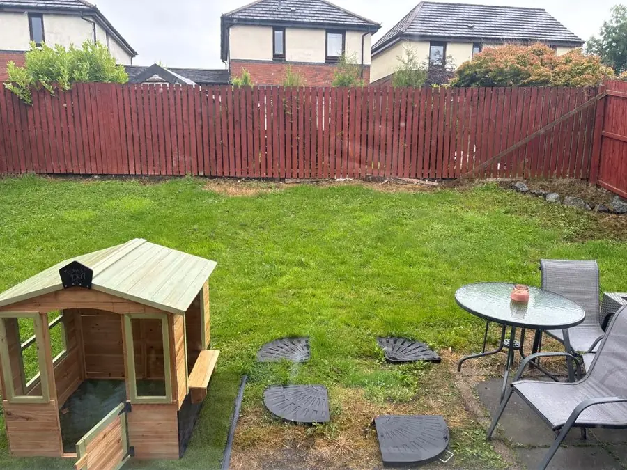 A lawn with a wooden playhouse, a glass table and a fence, before the redesign
