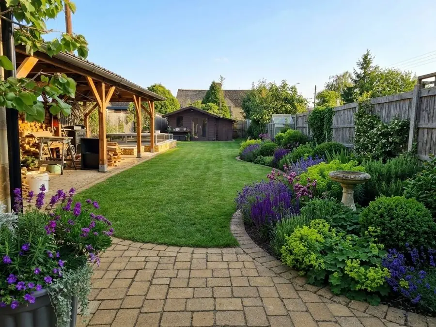 Block paving round an oval lawn, edged with lavender, lady's mantle and clipped balls, a patio garden idea