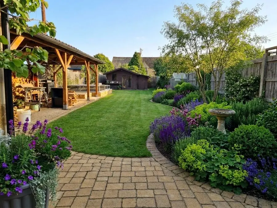 Box balls and a bird bath beside an oval lawn and block paving, an evergreen garden idea