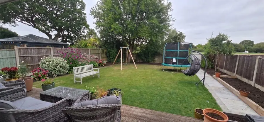 A family lawn with a swing and trampoline, a new fence and a border of shrubs, redesigned with the app