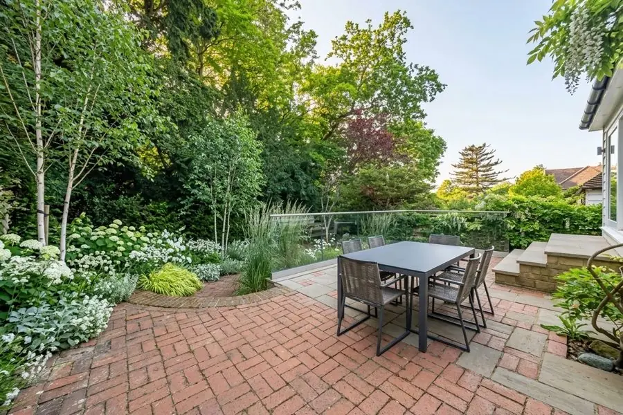 A weedy brick patio planted round with birches, ferns and white flowers, redesigned with the app